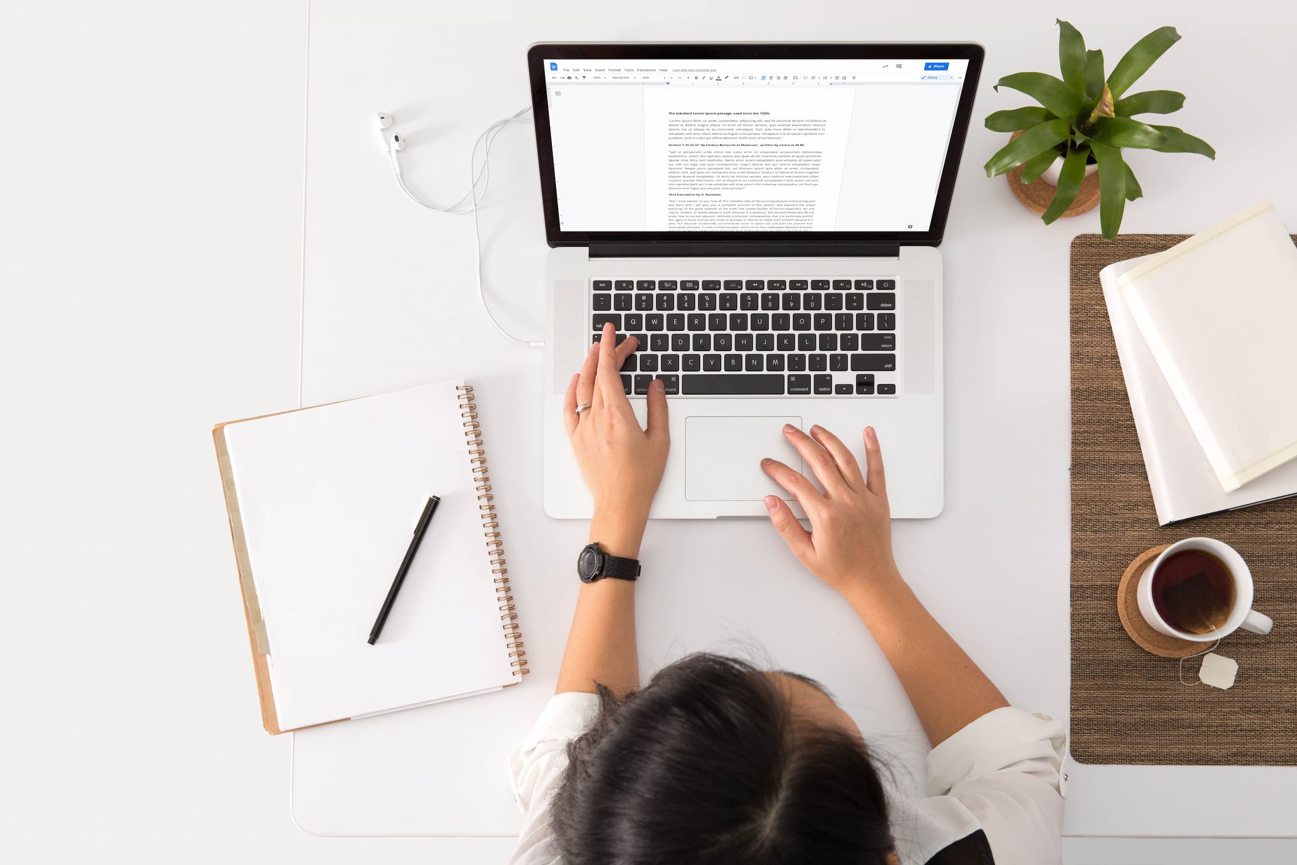 Woman typing on laptop with notepad and pen beside her.