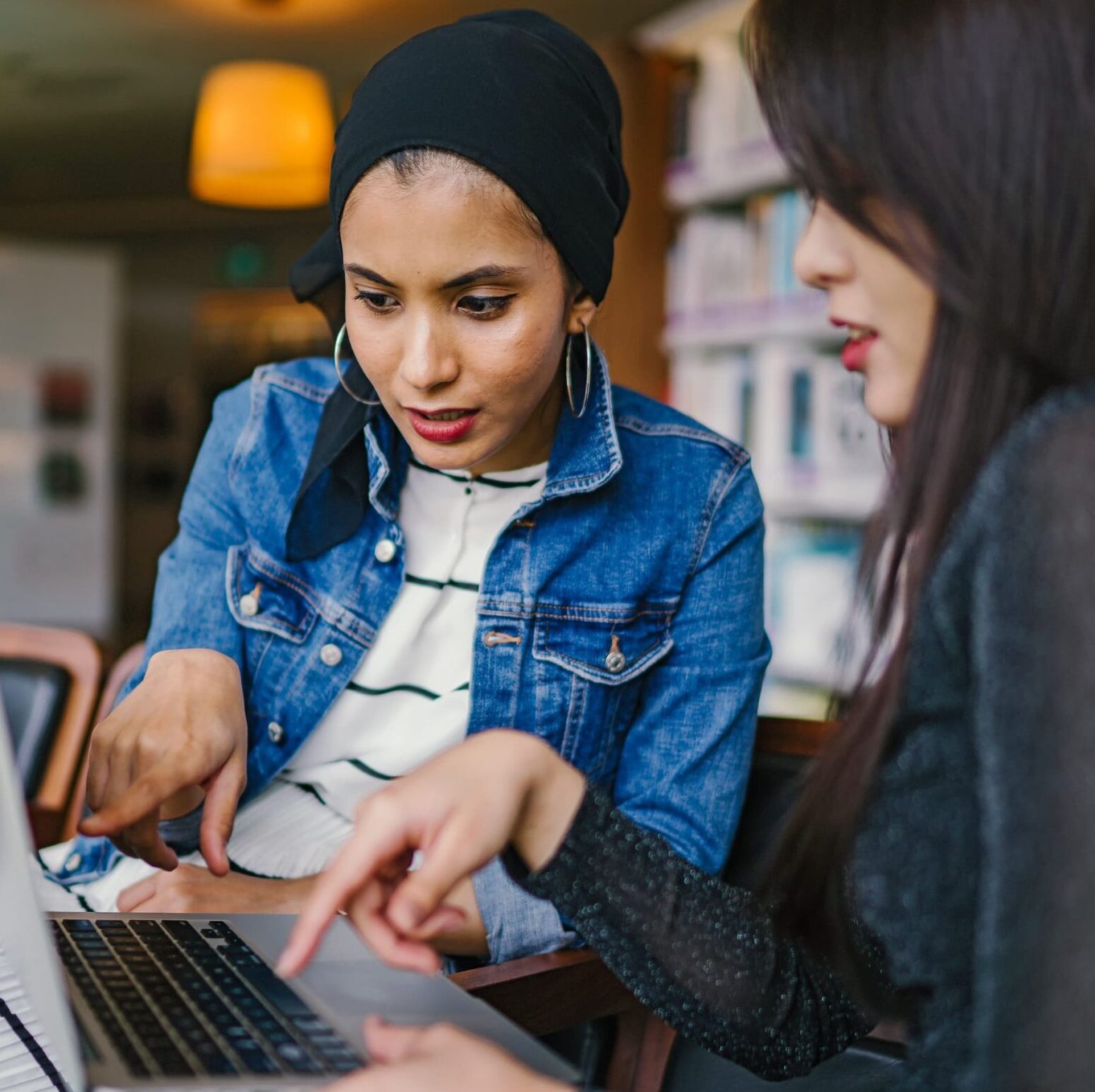 Two women looking at laptop screen and seem to be discussing something on the screen.