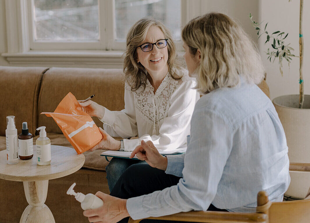 Two women sitting facing each other. One is holding a product and listening to the other speaking to her.