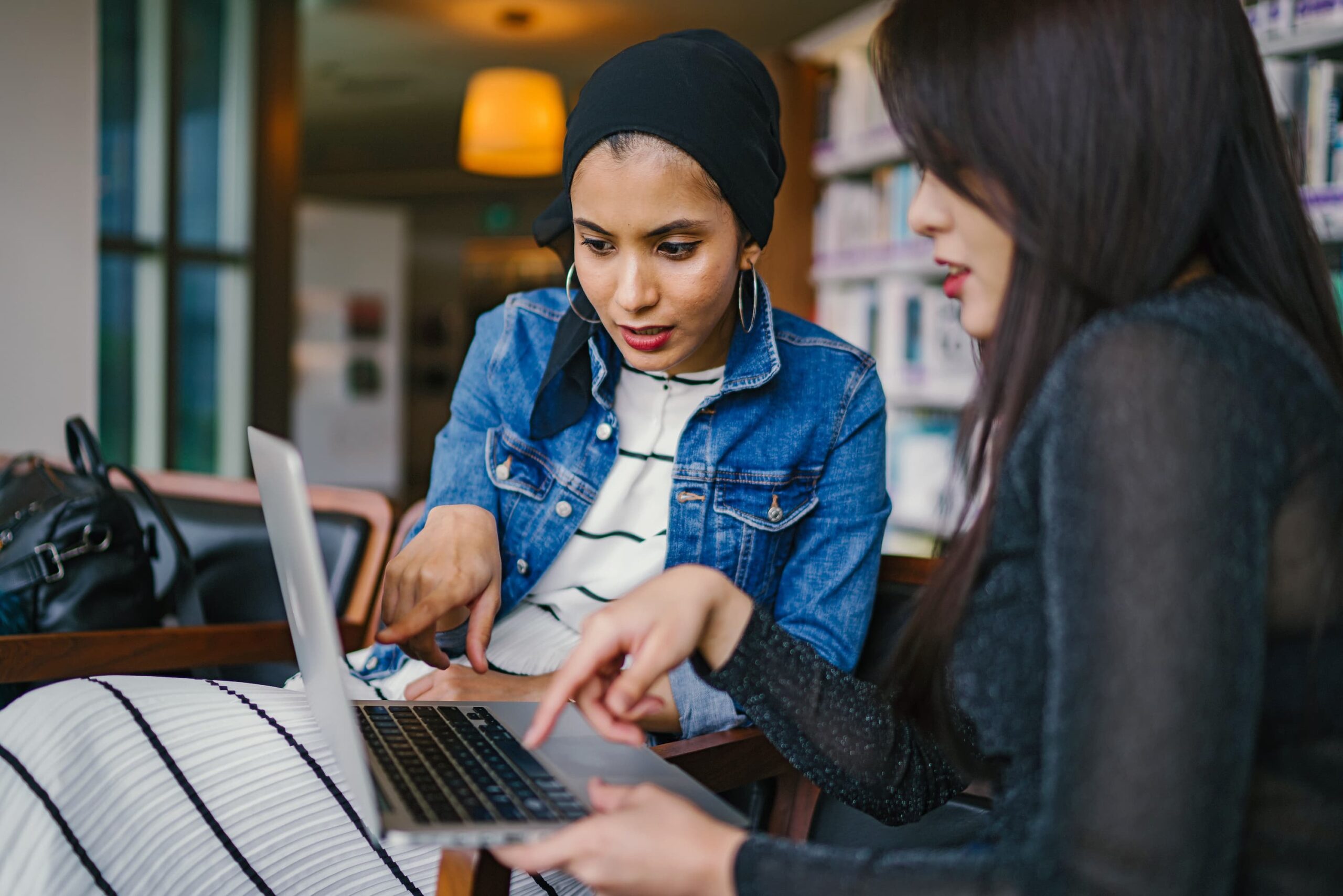 Two women looking at a laptop screen and speaking with each other.